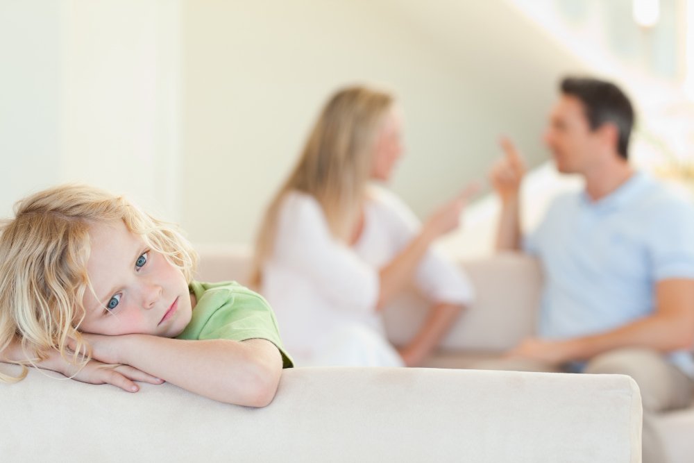 Niño triste observando a sus padres discutir, lo que refleja la importancia de educar a nuestros hijos con el ejemplo.