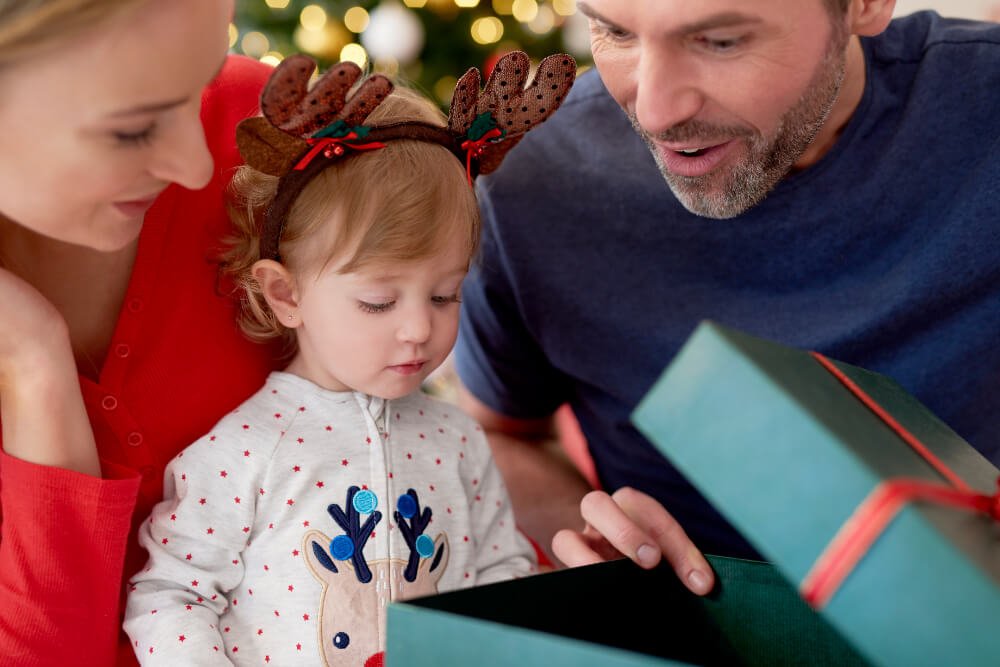 Familia feliz abriendo un regalo con su hija pequeña durante el día de Reyes en familia.